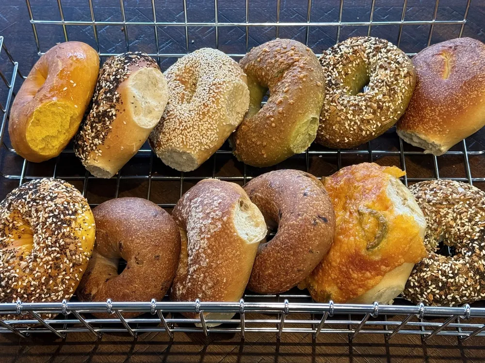 A wire rack of freshly baked East Coast style bagels in assorted flavours